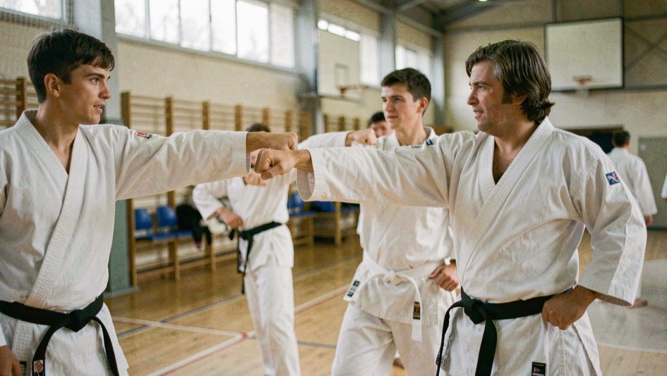 Rij karateka in witte pakken oefent gelijktijdig een vuiststoot langs de zijkant van een sportzaal